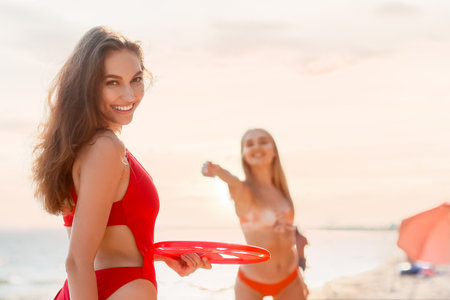 Beautiful young women playing frisbee on sea beachの写真素材