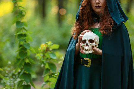 Young witch with skull in green forestの写真素材
