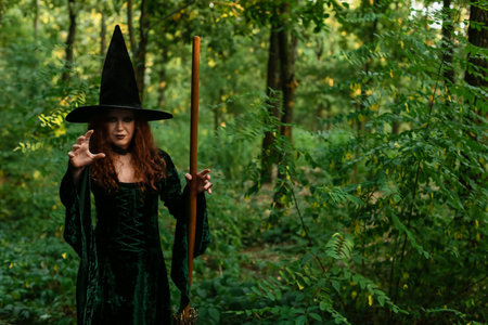 Young witch with broom in green forestの写真素材