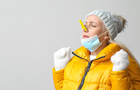 Ill mature woman with clothespin and medical mask on light background. stuffy nose concept