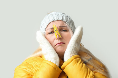 Ill mature woman with clothespin on light background, closeup. stuffy nose conceptの写真素材