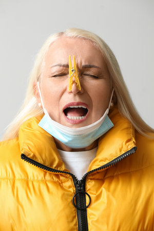 Ill mature woman with clothespin and medical mask on light background, closeup. stuffy nose conceptの写真素材