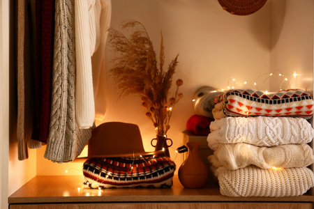 Warm knitted sweaters, hat, vases and glowing lights on shelf in wardrobeの写真素材