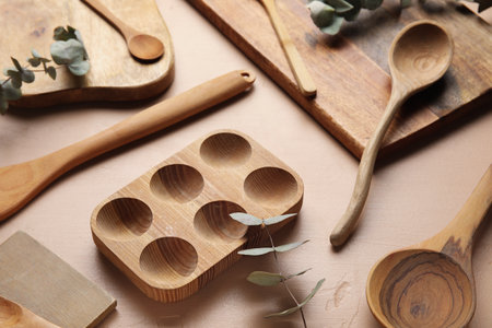 Wooden cooking utensils and eucalyptus branches on beige background, closeup