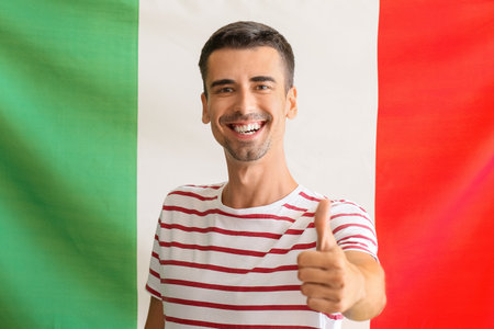 Handsome young man showing thumb-up against Italian flagの写真素材