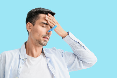Ill young man with clothespin on his nose against color background