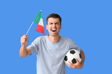 Emotional young man with Italian flag and soccer ball on color backgroundの写真素材