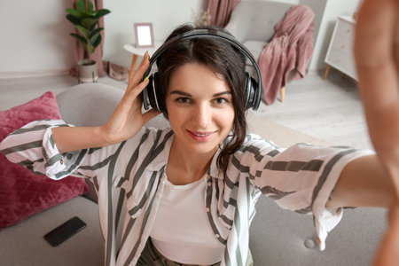 Beautiful brunette woman in headphones taking selfie at homeの写真素材