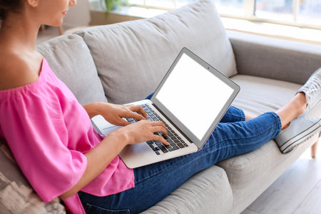 Young woman using laptop on sofa at homeの写真素材