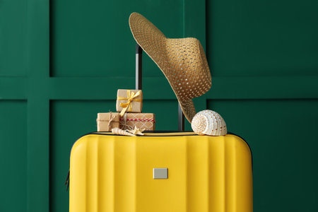 Suitcase with Christmas gifts, hat and seashells near green wallの写真素材