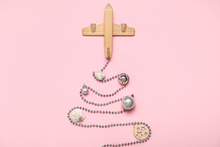 Wooden airplane with beads, seashells and Christmas balls on pink background