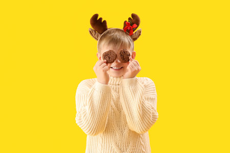 Happy little boy in reindeer horns with cookies on yellow backgroundの写真素材