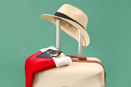 Suitcase with Santa hat and travel accessories on green backgroundの写真素材