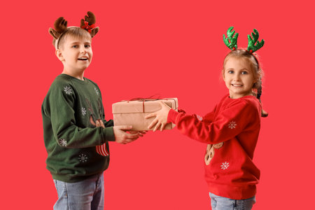 Happy little children in reindeer horns with Christmas gift on red background