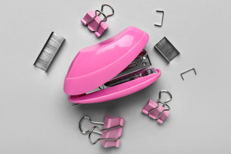 Pink stapler, staples and paper clips on light background