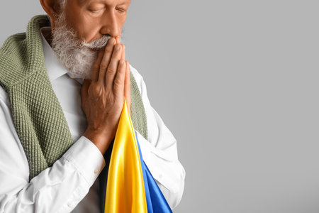 Mature man with flag of Ukraine praying on gray backgroundの写真素材