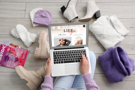 Female lifestyle blogger with laptop, magazines and clothes on light wooden floorの写真素材