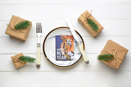 Table setting with greeting card for New Year 2022 celebration on white wooden background