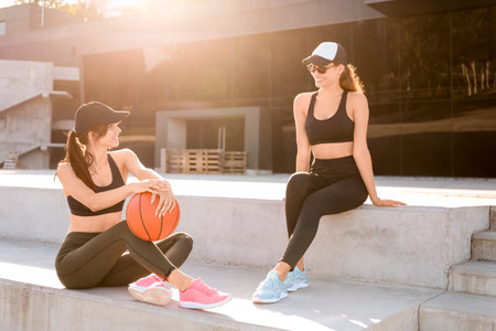Sporty young women with ball sitting on stairs outdoors