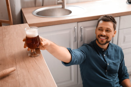 Handsome man taking glass of beer from kitchen counterの写真素材