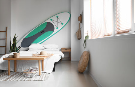Comfortable bed and sup surfing board on light wall in room interiorの写真素材