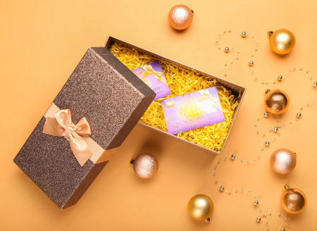 Box with gift cards and Christmas balls on beige background