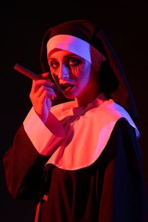 Woman dressed for Halloween as nun with cigar on dark backgroundの写真素材
