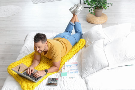 Handsome man working with laptop on bed at homeの写真素材