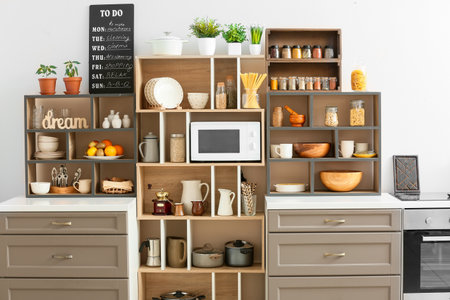Shelf unit with utensils and modern microwave oven in kitchen interior