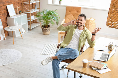 Happy young man talking by mobile phone in officeの写真素材