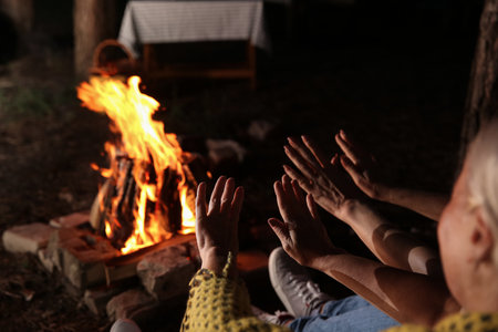 Mature women warming hands near fire on summer evening