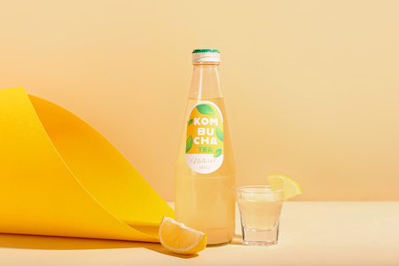 Bottle and shot of tasty kombucha tea with lemon on color background