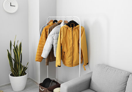 Rack with warm jackets near light wall in living room
