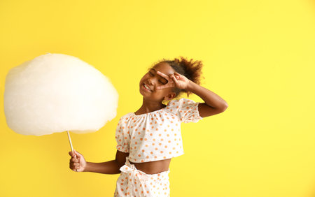 Little African-American girl with cotton candy on yellow backgroundの写真素材