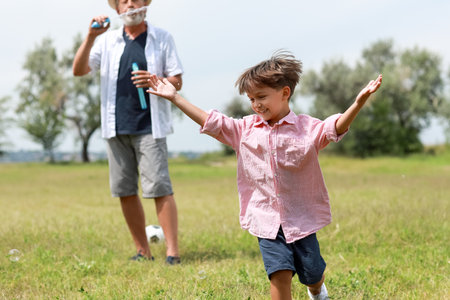 Little boy and his grandfather having fun with soap bubbles outdoorsの写真素材