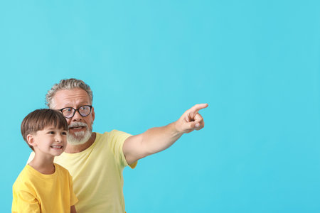 Little boy and his grandfather pointing at something on blue backgroundの写真素材