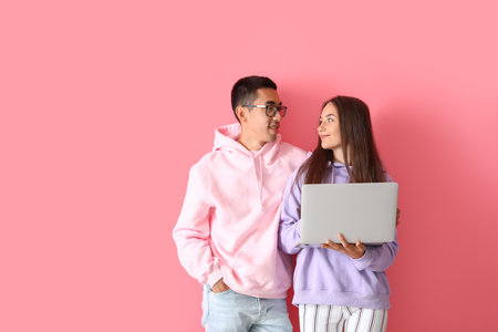 Young couple with laptop on pink backgroundの写真素材