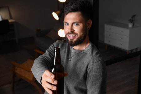 Young bearded man with bottle of beer at home in the eveningの写真素材