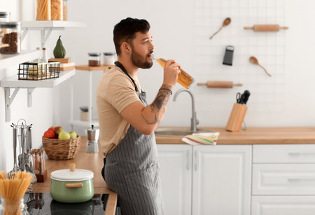 Young bearded man drinking beer in kitchenの写真素材