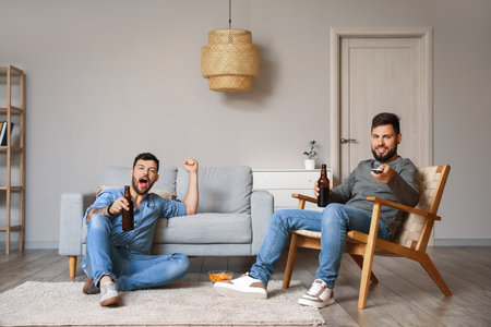 Male friends with bottles of beer watching TV at homeの写真素材