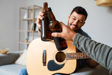 Male friends with bottles of beer and guitar at homeの写真素材
