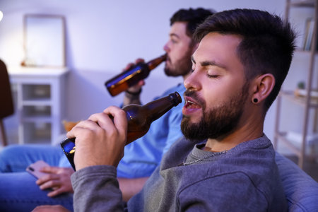Young bearded man drinking beer at home in the evening, closeupの写真素材