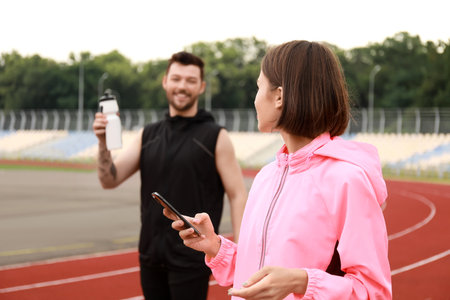 Sporty young woman with mobile phone and her husband at stadium