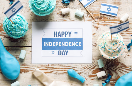 Card with text HAPPY INDEPENDENCE DAY, cupcakes and festive decor on light wooden backgroundの写真素材