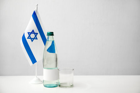 Bottle with water and flag of Israel on table near light wallの写真素材