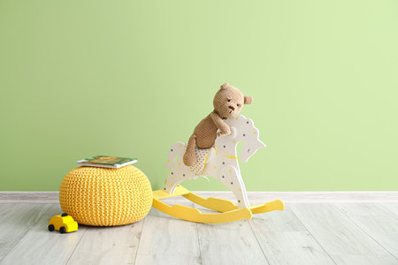Toy bear sitting on rocking horse, pouf with books and car near color wallの写真素材