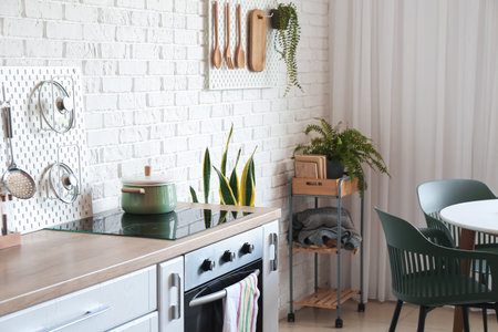 Cooking pot on stove and pegboard with utensils near white brick wall in kitchen interior