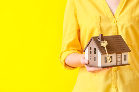 Young woman with house model and key on yellow background, closeupの写真素材