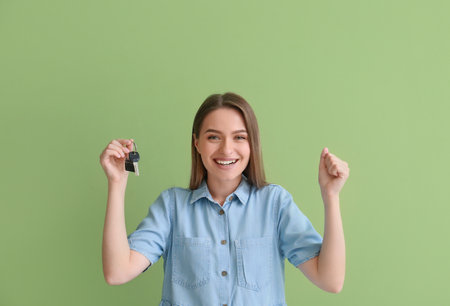 Happy young woman with key from house on green backgroundの写真素材