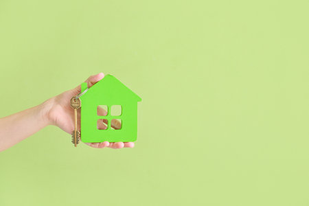 Young woman with key from house on green backgroundの写真素材